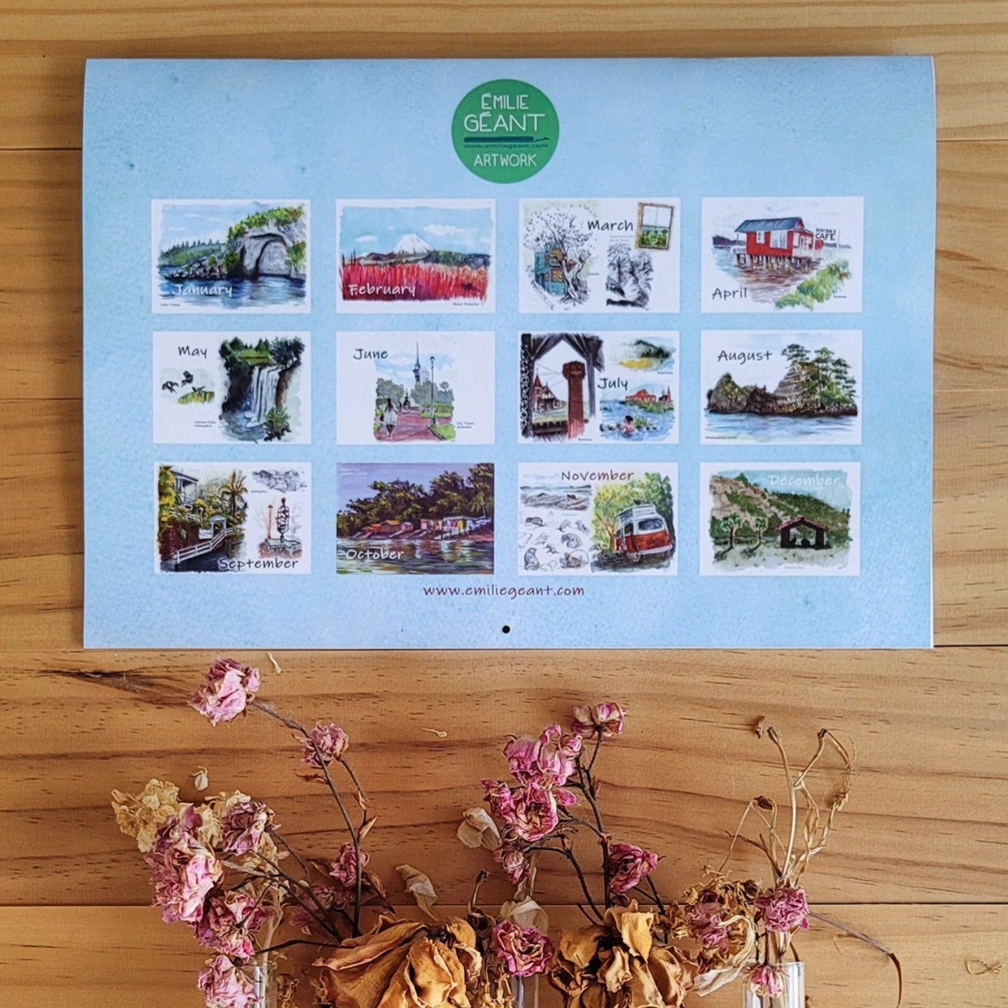 Calendar with monthly illustrations on a wooden surface with flowers.
