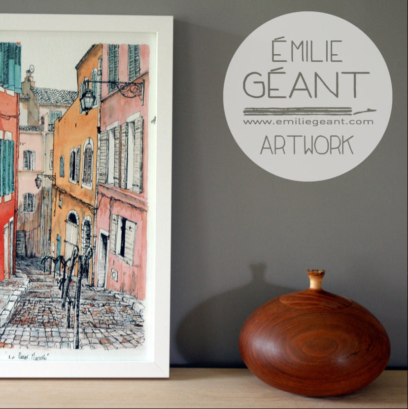 Framed artwork of a street scene with 'Emilie Géant' branding on a gray wall.